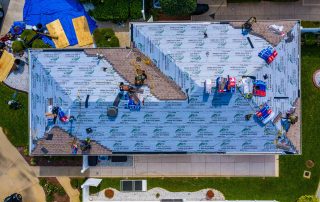 Aerial view of workers installing roofing materials and equipment on a house roof under renovation.