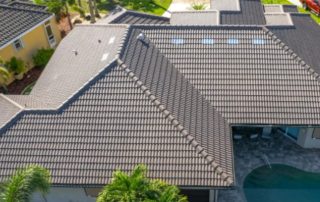 Aerial view of a house with a dark gray tile roof, multiple roof angles, and a backyard swimming pool.